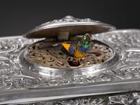 The Rococo design of the sterling silver musical bird box shown here typifies the elaborate mechanism and design work prevalent in that era.  The filigree design and scroll work hides a brightly feathered bird which pops out and chirps a song and flutters its wings before disappearing back into the box.  