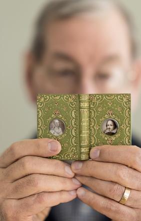 Neale Albert holding 3" book “Julius Caesar” bound by Santiago Brugalla, 2004, one of the volumes of the Knickerbocker set of Shakespeare.  Bound in green goatskin, with gold and red tooling.  Miniature portrait medallions, painted by John Hodgson, on front and back covers in imitation of a Cosway-style binding.  