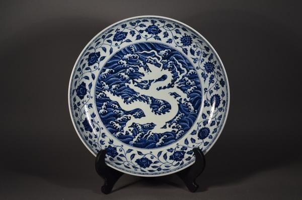 Lot 502: Important and rare, large 15th Century Chinese Ming Dynasty porcelain charger; central reverse design of writhing dragon amid crashing waves, surrounded on the cavetto with a continuous band of lotus blossoms borne on a single undulating stem with lobed leaves; the exterior with a band of five-toed dragons chasing flaming pearls; six-character Xuande Mark and of the Period; D: 49 cm, H: 9 cm (Estimate: $150,000-250,000) 