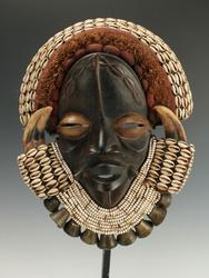 African Dan Guere mask, 23 inches by 10 inches, made from wood, wild boar horn, cowrie shells, beads, textiles, raffia and bronze bells, on a custom stand (est.  $300-$500).