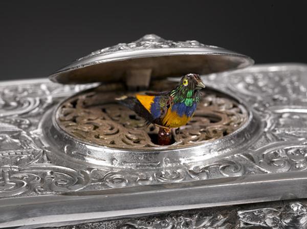 The Rococo design of the sterling silver musical bird box shown here typifies the elaborate mechanism and design work prevalent in that era.  The filigree design and scroll work hides a brightly feathered bird which pops out and chirps a song and flutters its wings before disappearing back into the box.  