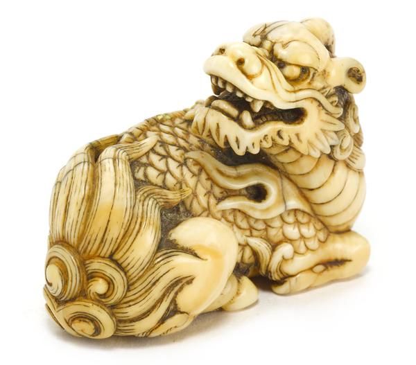 An ivory netsuke of a recumbent kirin By Okatomo, Kyoto, Edo period (late 18th/early 19th century) The mythical animal shown reclining, looking back over its right haunch with its mouth open in a snarl, its tail laying over its hips and its feet tucked in beneath its body forming a compact design, the details finely carved and stained dark, eyes inlaid in dark horn, signed in a rectangular reserve Okatomo 1 7/8in (4.8cm) long Est US$ 25,000 - 35,000