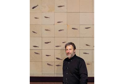 Douglas Miller stands in front of a wall mural composed of fish fossils.