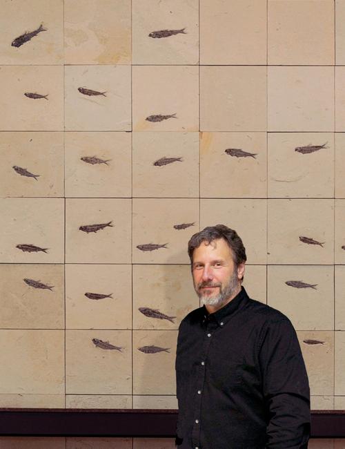 Douglas Miller stands in front of a wall mural composed of fish fossils.