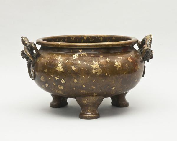 A large cencer, from 17th century China, standing on three cabriole feet, decorated with irregular gilt splashes.  The handles formed as crouching dragons.  The base cast features the Xuande mark.  (from Brandt Asian Art)