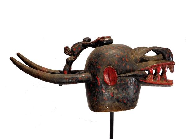 Senufo Kulonugo fire spitter, a massive wood carving covered with black paint and adorned by additions of red paint.  Atop the head is a carved offering bowl (est.  $2,500-$5,000).