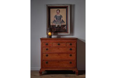 Folk Portrait of a Boy with Whip and Pull Toy on a Patterned Ground above a Pennsylvania Chippendale Chest of Drawers retaining a vibrant grain-painted finish