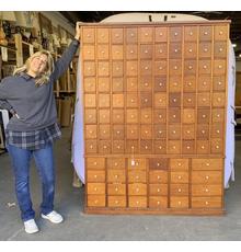 Pam Stone stands next to this rare and massive 104-drawer apothecary library card filing cabinet ($400-800) with hand dovetailing and porcelain knobs, which stands over 72 inches tall.