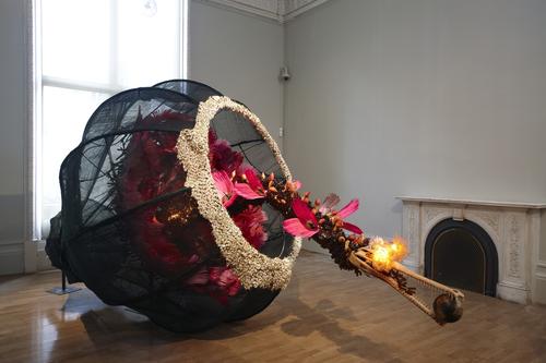 Rina Banerjee, The world as burnt fruit—When empires feuded for populations and plantations, buried in colonial and ancient currency a Gharial appeared from an inky melon—hot with blossom sprang forth to swallow the world not yet whole as burnt fruit, 2009.  Fans, feather, cowrie shells, resin alligator, skull, globe, glass vials, light bulbs, gourds, steel wire and Japanese mosquito nets, 90 × 253 × 90 inches.  Kiran Nadar Museum of Art, New Delhi, India.