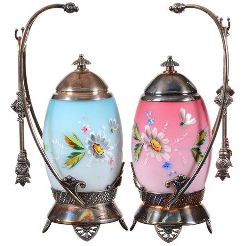 Matched pair of 9.5-inch pickle castors, one having a blue satin art glass finish, the other a pink satin art glass insert and both boasting enamel floral decor.